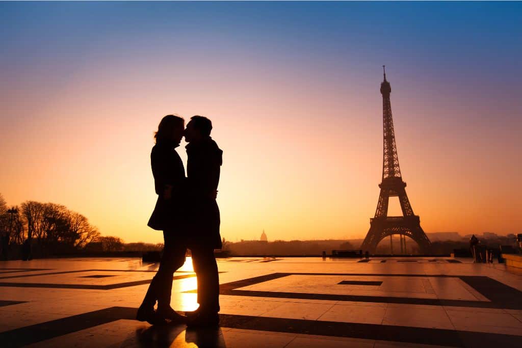 a couple embraces at sunset in front of the Eiffel Tower in Paris, France, perhaps the most romantic city in Europe