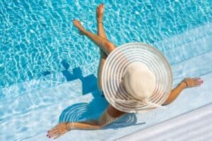 a woman with a large white sun hat sits in the clear blue water