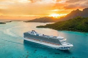 a Princess cruise ship sails on a turquoise sea in an exotic locale with orange sunset and mountains in the background